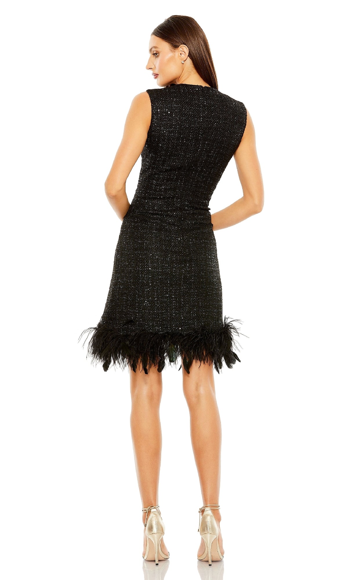 A woman faces away, wearing the Mac Duggal 20784 short black shimmer party dress with a feather-trimmed hem and silver high-heeled sandals, standing against a white background.